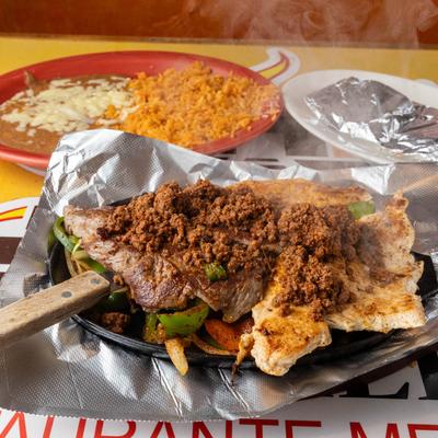 Grilled chicken breast and steak with sausage and peppers, served with rice and beans.