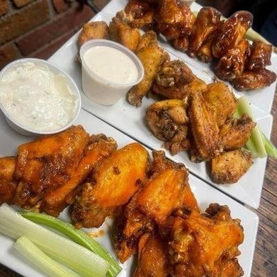 Three plates of chicken wings served with celery sticks and dipping sauces.