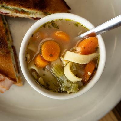 Chicken noodle soup with carrots and celery beside a toasted sandwich.