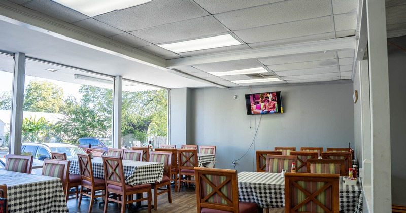 Interior, tables for dining covered with patterned table cloths, chairs and  a TV