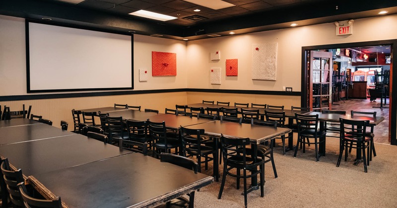 Room with long tables and seats and a projection screen on the wall