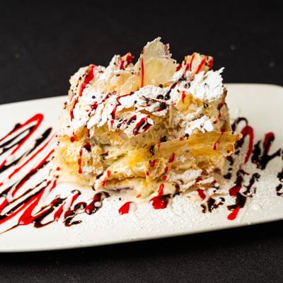 Napoleon cake dusted with powdered sugar, drizzled with chocolate and berry sauces.