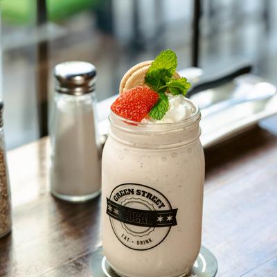 Strawberry short shake served in a Green Street Local glass jar on a table by a window.