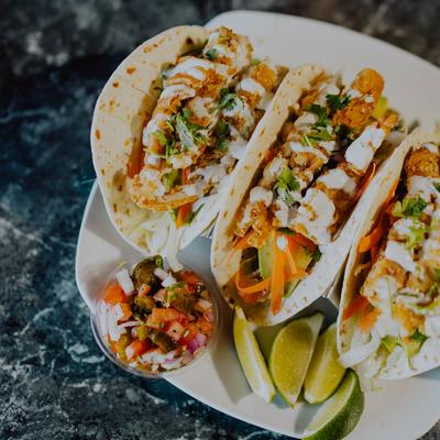 Three fried chicken tacos served with fresh salsa and lime wedges.