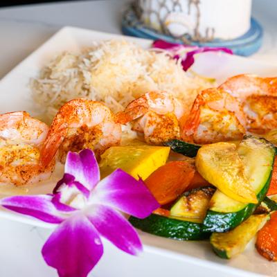 Grilled shrimp with rice, sauteed vegetables, and orchid garnish.