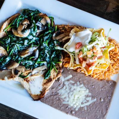 Spinach chicken served with a taco salad, rice, and refried beans topped with cheese.