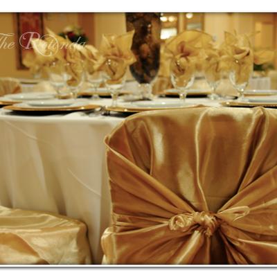 Elegant gold satin chair covers and napkins accent a formal white-clothed table.
