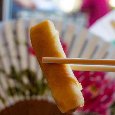 A veggie spring roll held up by chopsticks with a colorful background, close up.