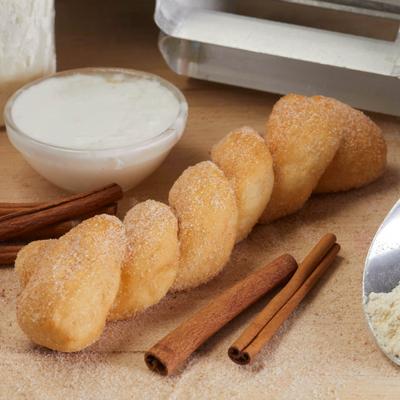 Glazed twist beside cinnamon sticks on a wooden board.