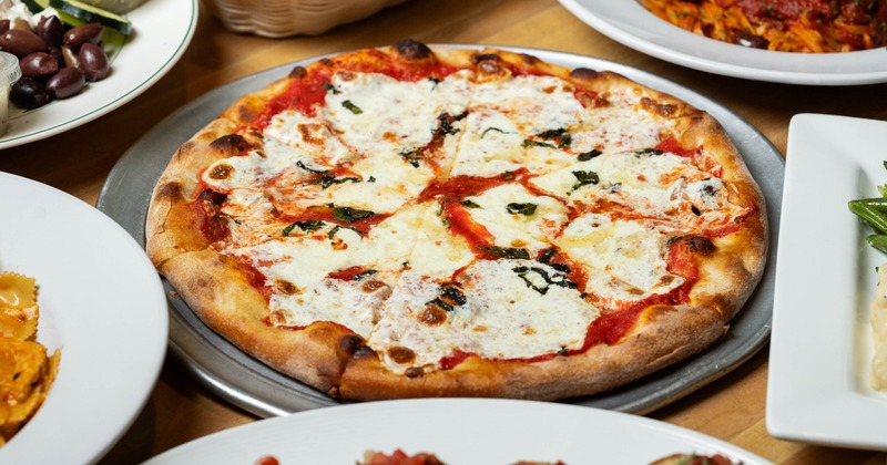 Margherita pizza on a metal tray, surrounded by various other Italian dishes