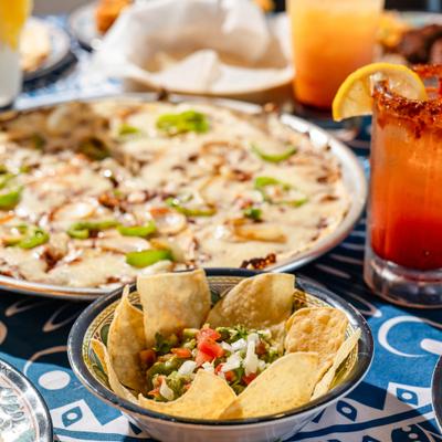 Guacamole with tortilla chips, served alongside various dishes and cocktails.