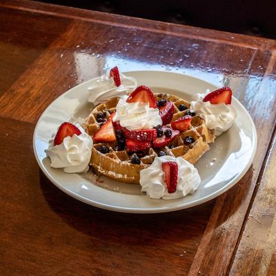 Plate of waffles topped with sliced strawberries, blueberries, and whipped cream on a wooden table.
