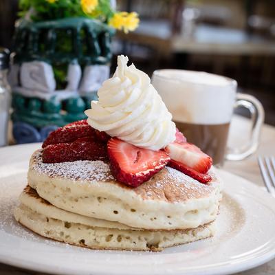 Fluffy pancakes with whipped cream and sliced strawberries on top.