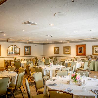 Elegant banquet room with set round tables, framed artwork, and a table with chafing dishes.