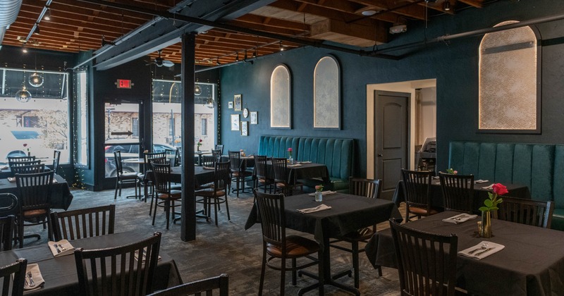 Cozy interior, dark decor, elegant lighting, featuring tables with black tablecloths and pink roses