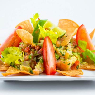 Shrimp ceviche with tomato wedges, lime garnish, celery leaves, and crispy tortilla chips.