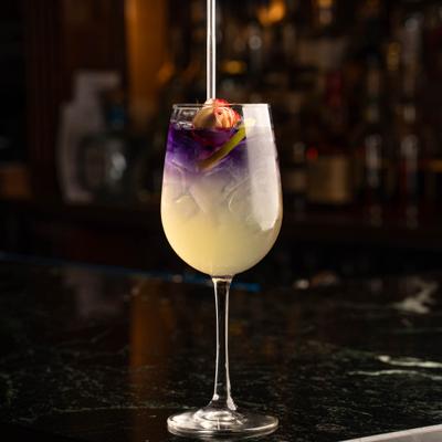 Layered  cocktail in a wine glass, garnished with an flower and slice of lime.