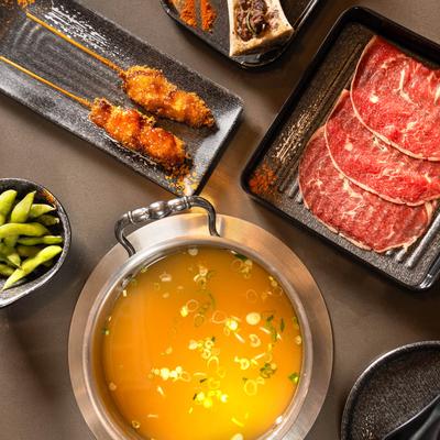 Hot pot broth surrounded by sliced beef, skewers, and small plates.