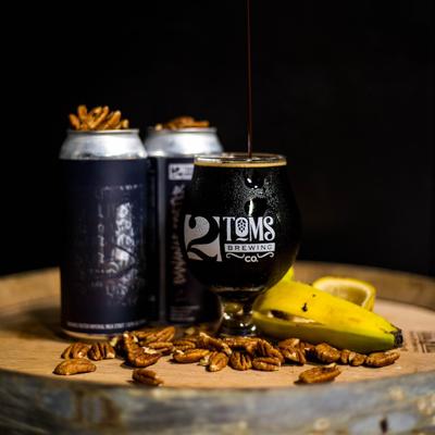 Stout glass and cans arranged on a  barrel top with tossed pecans and a banana peel.