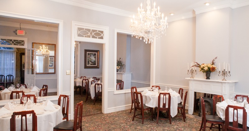 Set tables in a banquet room with white walls,  decorated fireplaces  and crystal chandeliers