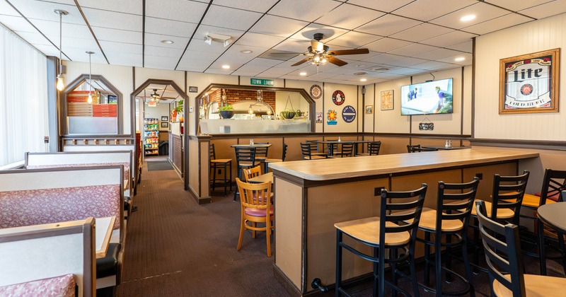 Interior of a restaurant with booths, a bar with stools, and wall decorations including a TV