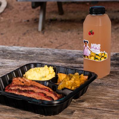 Barbecue brisket with sides and a bottle of raspberry lemonade on a picnic table.