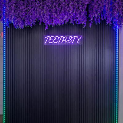 A neon sign with the words Teetasty in purple and purple flowers.