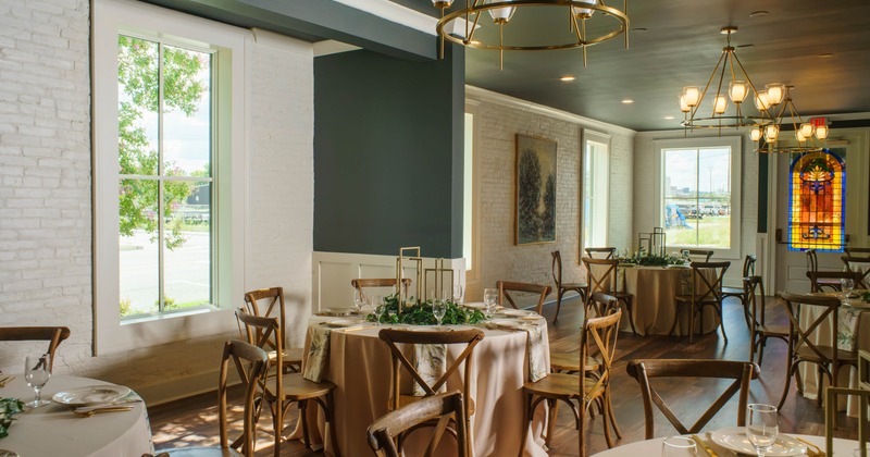 Interior, dining area, round tables for seven with cream colored cloths and wooden chairs