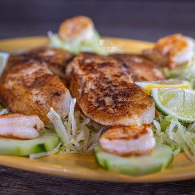 Tilapia fillets, seasoned shrimp, lettuce, and cucumbers, close-up.