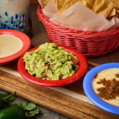 Chunky guacamole, cheese dip, and chorizo queso dip served with a basket of tortilla chips.