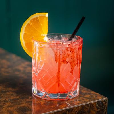 A pink citrus cocktail with an orange slice in a patterned rocks glass.
