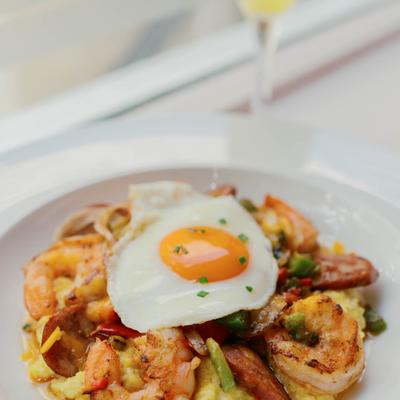 Breakfast bowl with shrimp, sausage, grits, bacon, cheese, and a fried egg