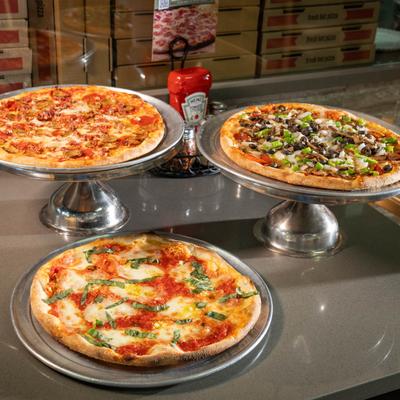 Three pizzas on metal stands atop a gray table, margherita, meat lovers, and Marina's supreme.