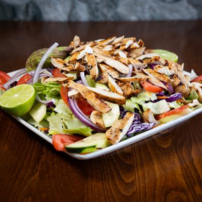 Grilled chicken salad with vegetables and lime on a square plate.