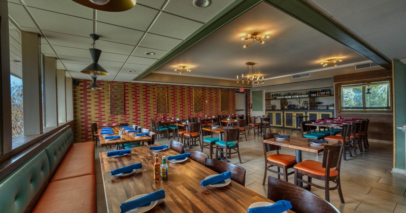 Interior of a restaurant with wooden tables set with blue napkins and various seating