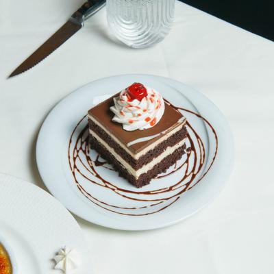 Chocolate layered cake slice with whipped cream and cherry.