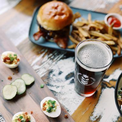 Beer with deviled eggs, cucumbers, and a burger with fries on a rustic table.