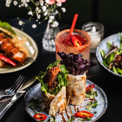 Duck roti wraps served with a cocktail and side dishes.