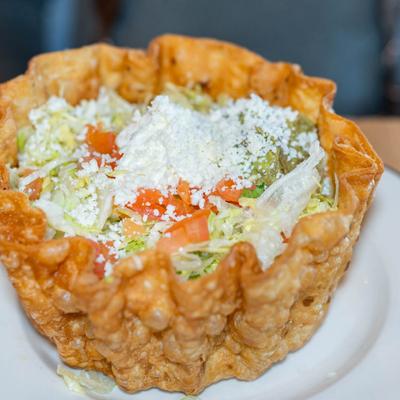 Taco salad in a tortilla bowl, with lettuce, tomato, cheese, sour cream, and guacamole.