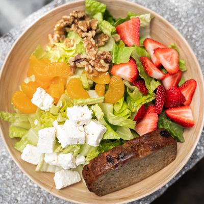 Salad with lettuce, strawberries, mandarin oranges, walnuts, feta, and bread.