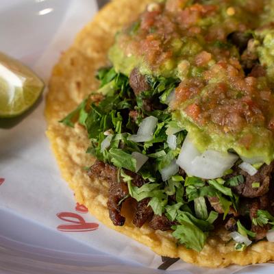 Carne asada taco with guacamole, salsa, cilantro, and onions.