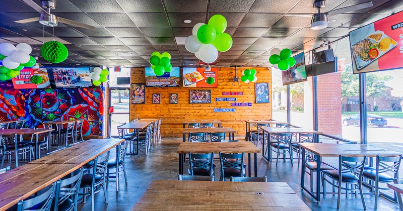 Interior of a festive restaurant with wooden tables, metal chairs, murals, and large windows