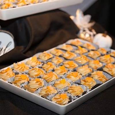 A tray of small cupcakes with swirled orange and cream frosting is displayed on a black fabric.