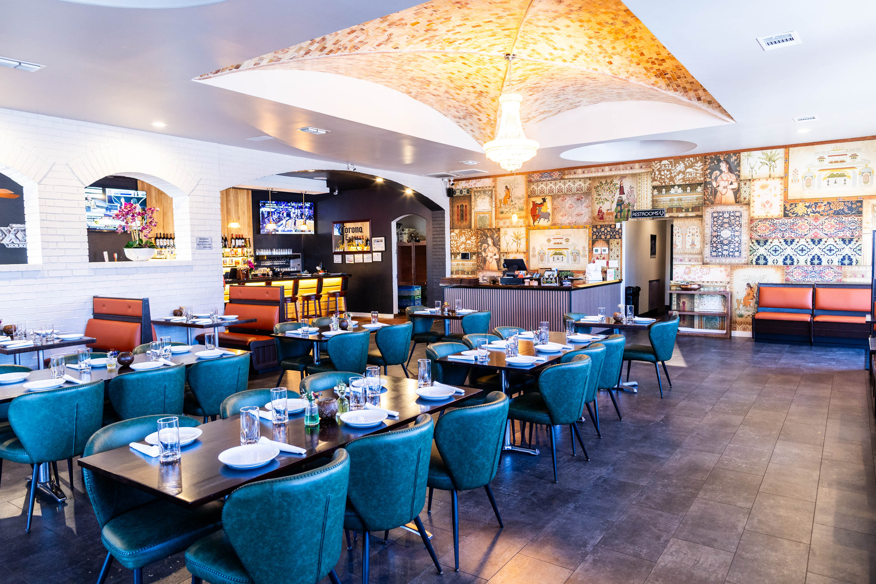 Modern interior with teal chairs, set tables, a bar and decorative wall art.