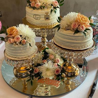 Three cakes with floral garnish  arranged on table covered  with white tablecloth.
