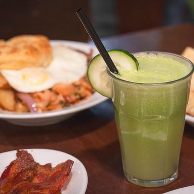 Fresh-squeezed juice garnished with a cucumber slice, surrounded by plates of food.