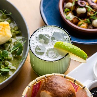 Classic margarita cocktail with lime garnish surrounded by plates of food.