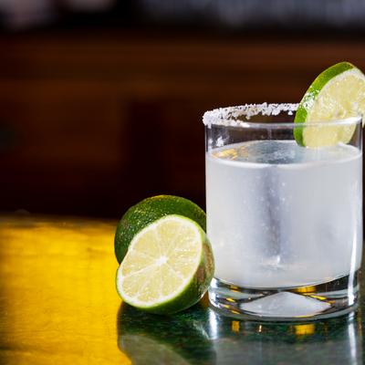 Salt-rimmed lime cocktail in short glass with fresh lime halves nearby.