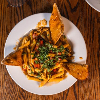 Chipotle Chicken Penne served on a wooden table with garlic bread.