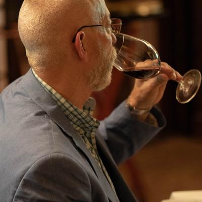 Man in a blue blazer tasting red wine indoors.